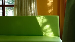 A green sofa in a room with a window, curtains, and a partial view of a wall. - Kasemsuk Resort (Bang Saphan)