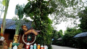 A traditional Thai village scene with a large Buddha statue, a decorative wheel, and a signboard. - Kasemsuk Resort (Bang Saphan)