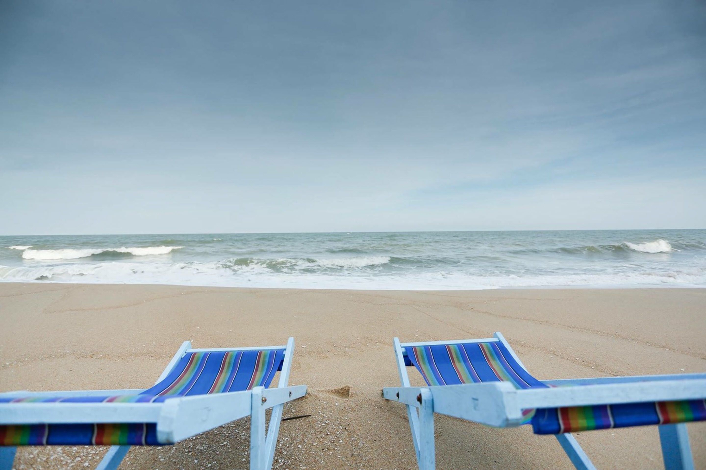 Two beach chairs facing the ocean with waves crashing onto the shore.