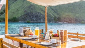 Ein Holztisch ist für das Frühstück gedeckt, mit Blick auf einen See und Hügel.