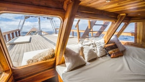 Eine Holzterrasse mit einem Bett und Kissen, Blick aufs Meer und einem wolkenlosen Himmel.