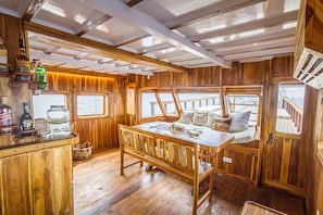 A wooden interior with a wooden bench, a table, and a bar area with bottles. - Kelana Boat (Labuan Bajo)