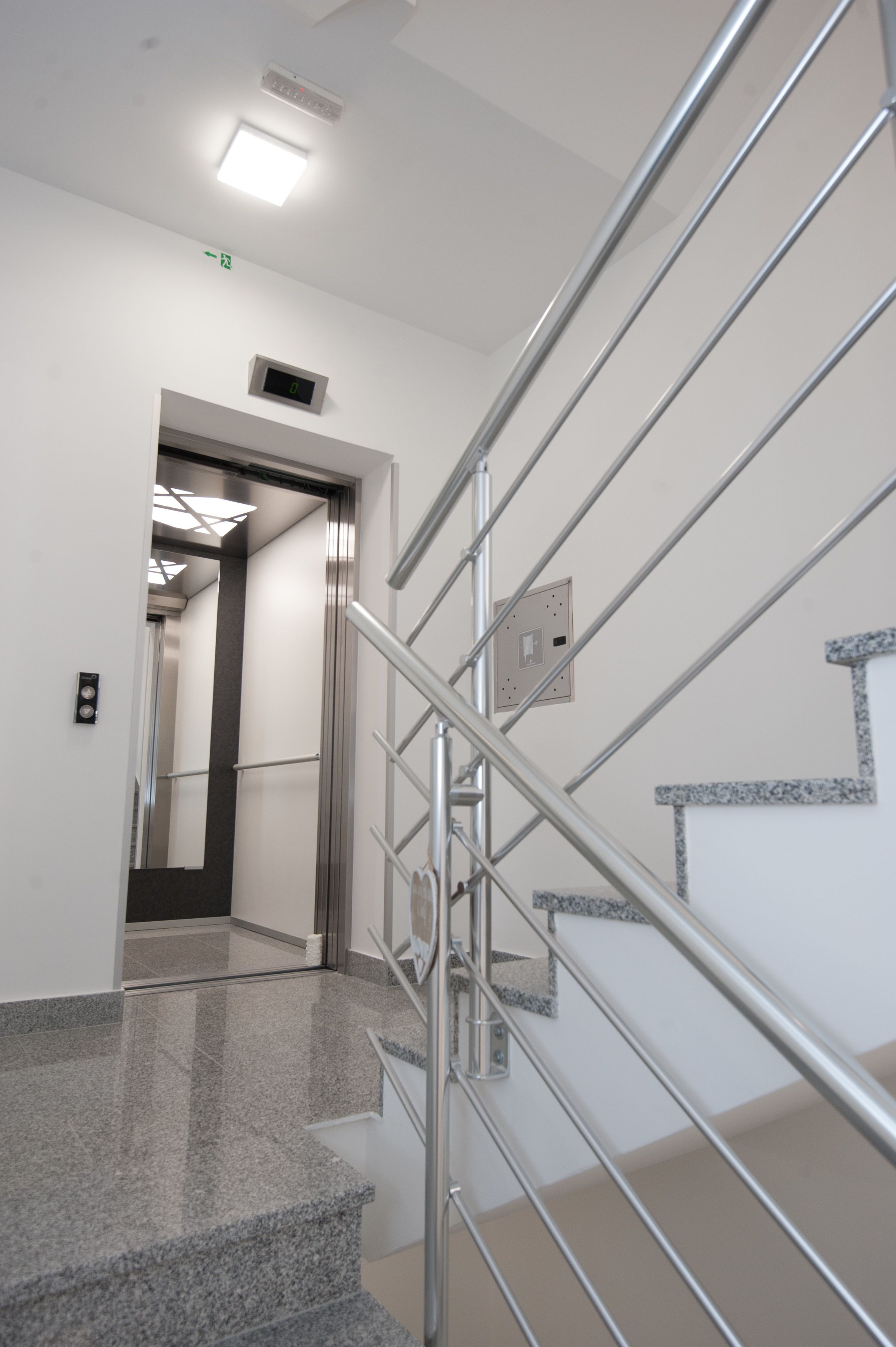 Una escalera moderna con barandillas metálicas y un reloj digital en la pared.