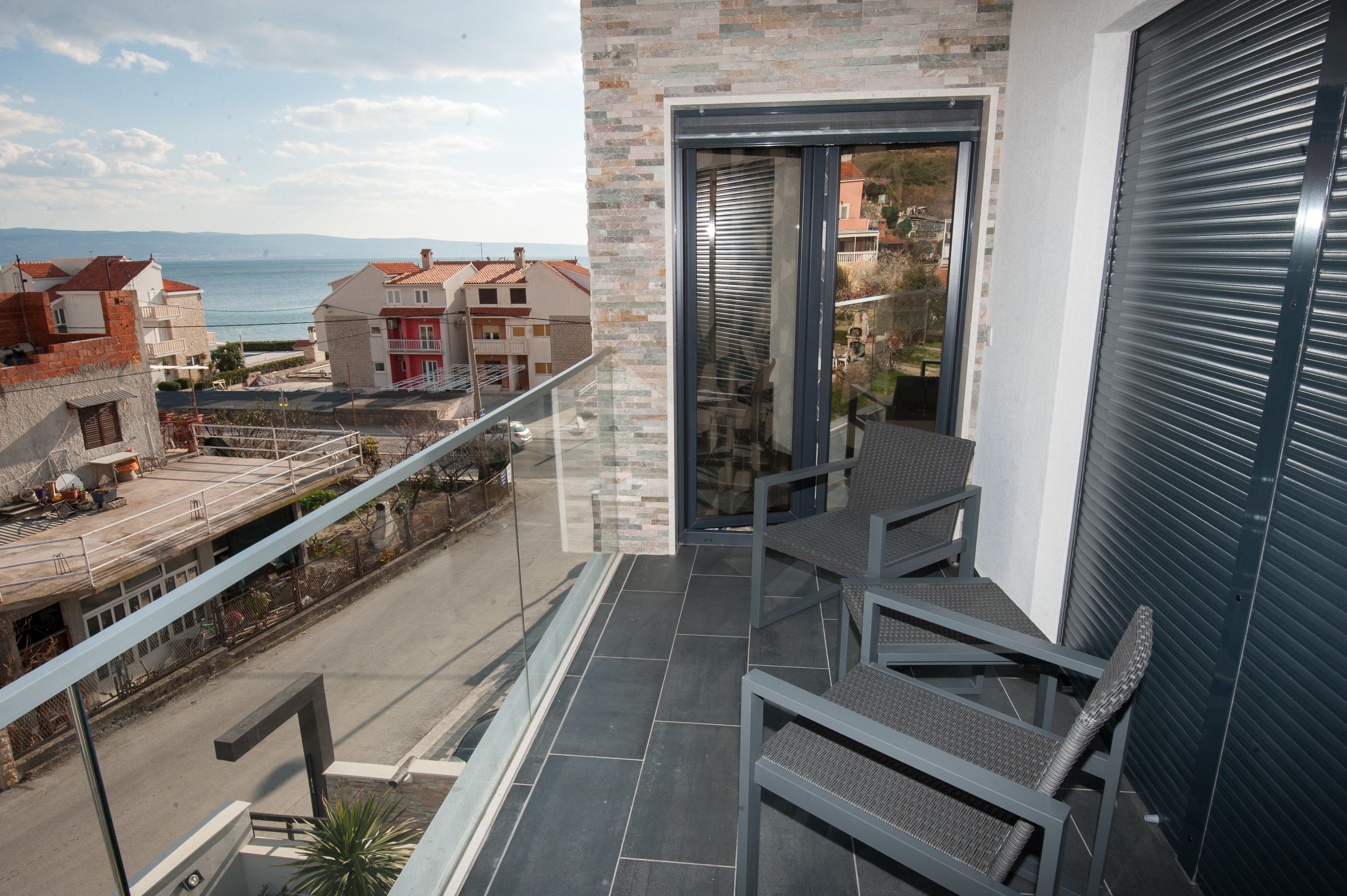 Een balkon met uitzicht op zee, een glazen deur en een metalen hekwerk.