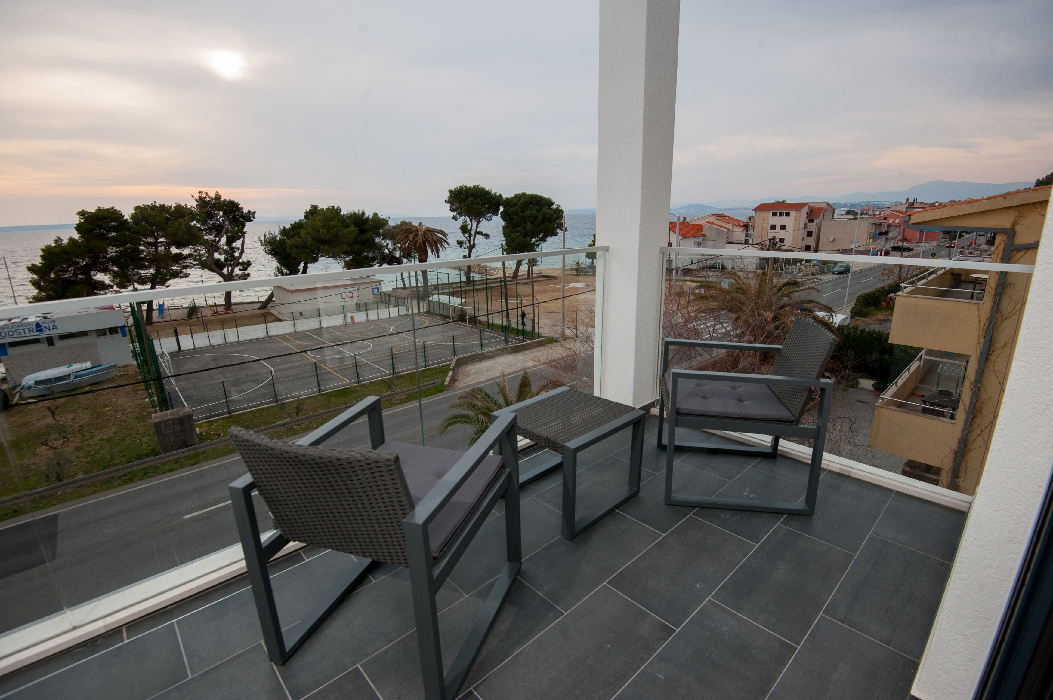 Un balcón con vistas al mar, una cancha de tenis y edificios circundantes.