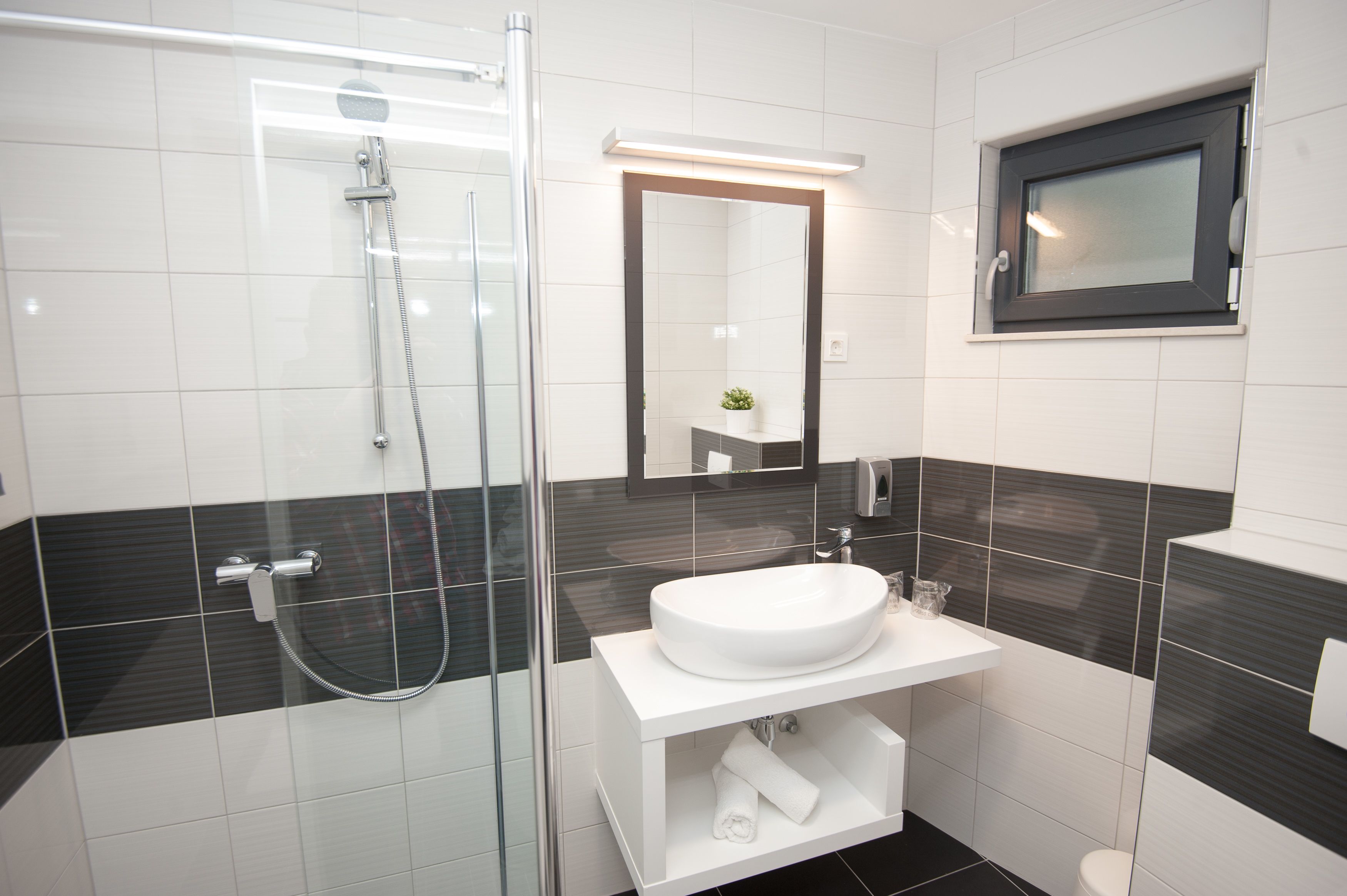 A modern bathroom with a glass-enclosed shower, a white sink, and a mirror with a small window above it.