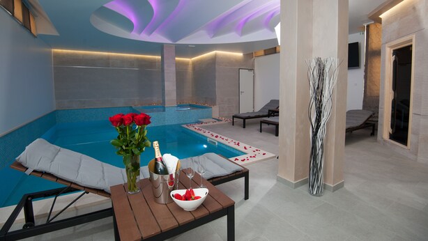 Una piscina interior moderna con zona de descanso, una mesa con una botella de champán y un jarrón con rosas rojas.