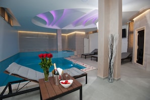 A modern indoor swimming pool with a lounge area, a table with a bottle of champagne, and a vase of red roses.