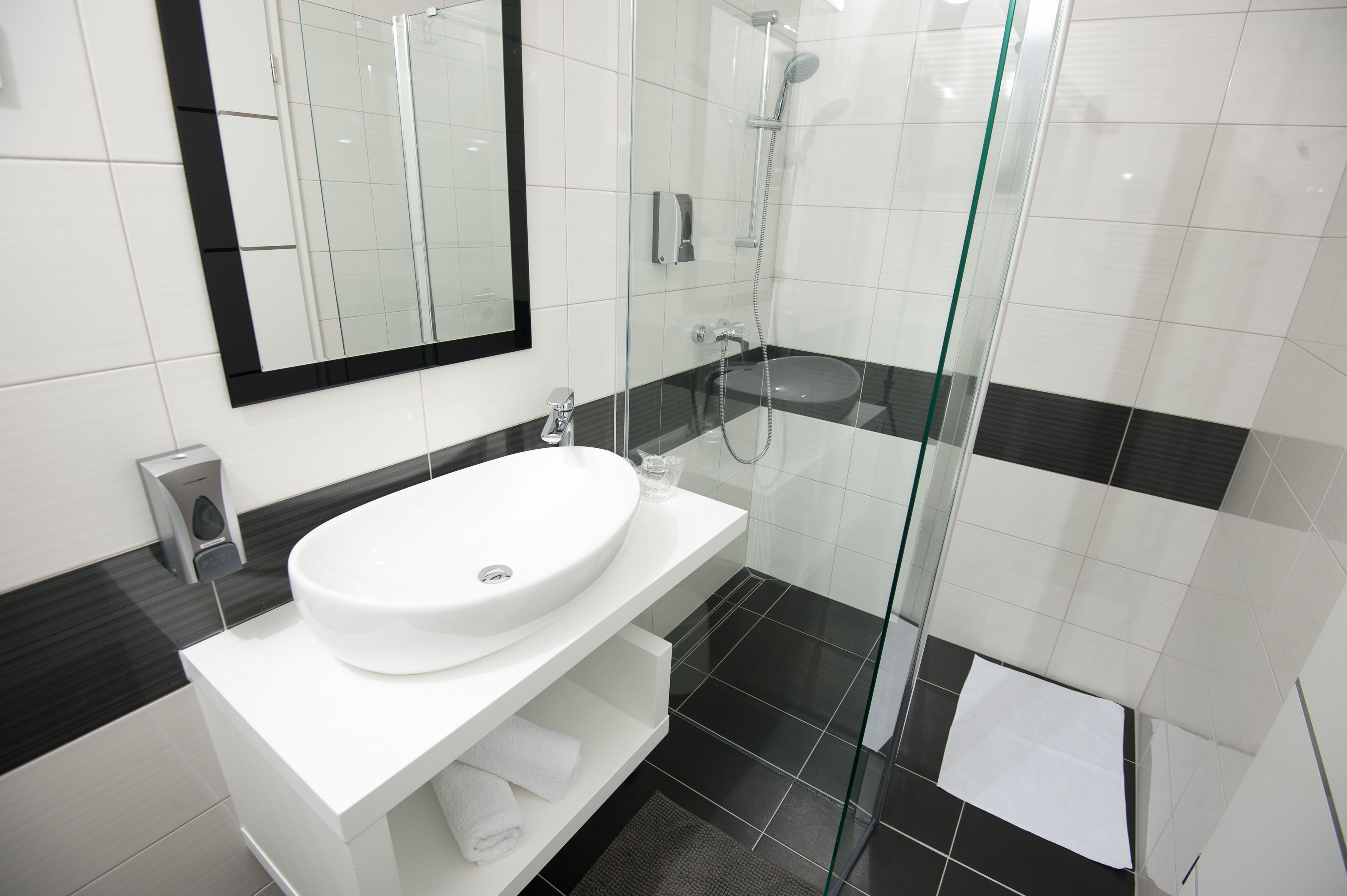 Une salle de bain moderne avec un lavabo blanc, une douche en verre et un sol carrelé en noir et blanc.