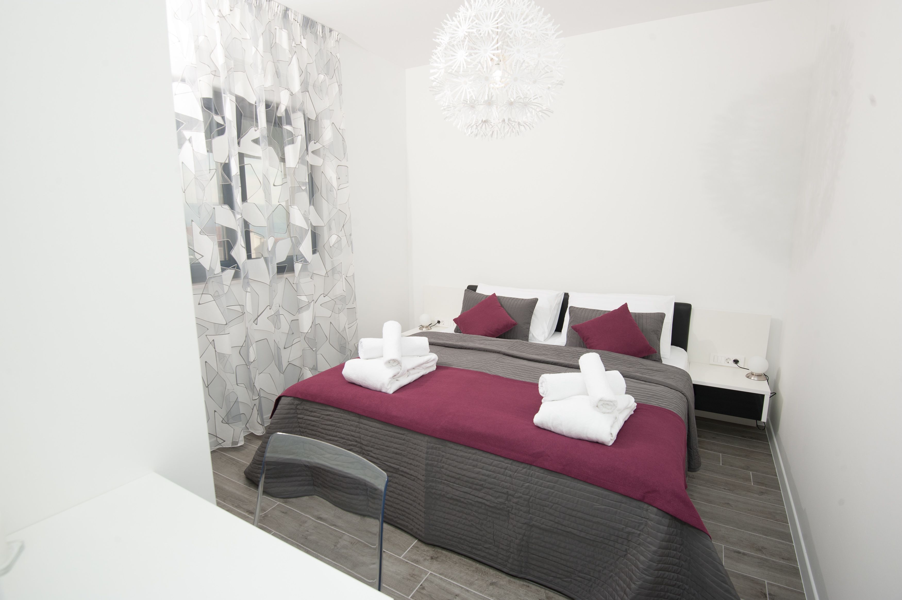 A modern hotel room with a large bed, two bedside tables, a chair, and a decorative chandelier.