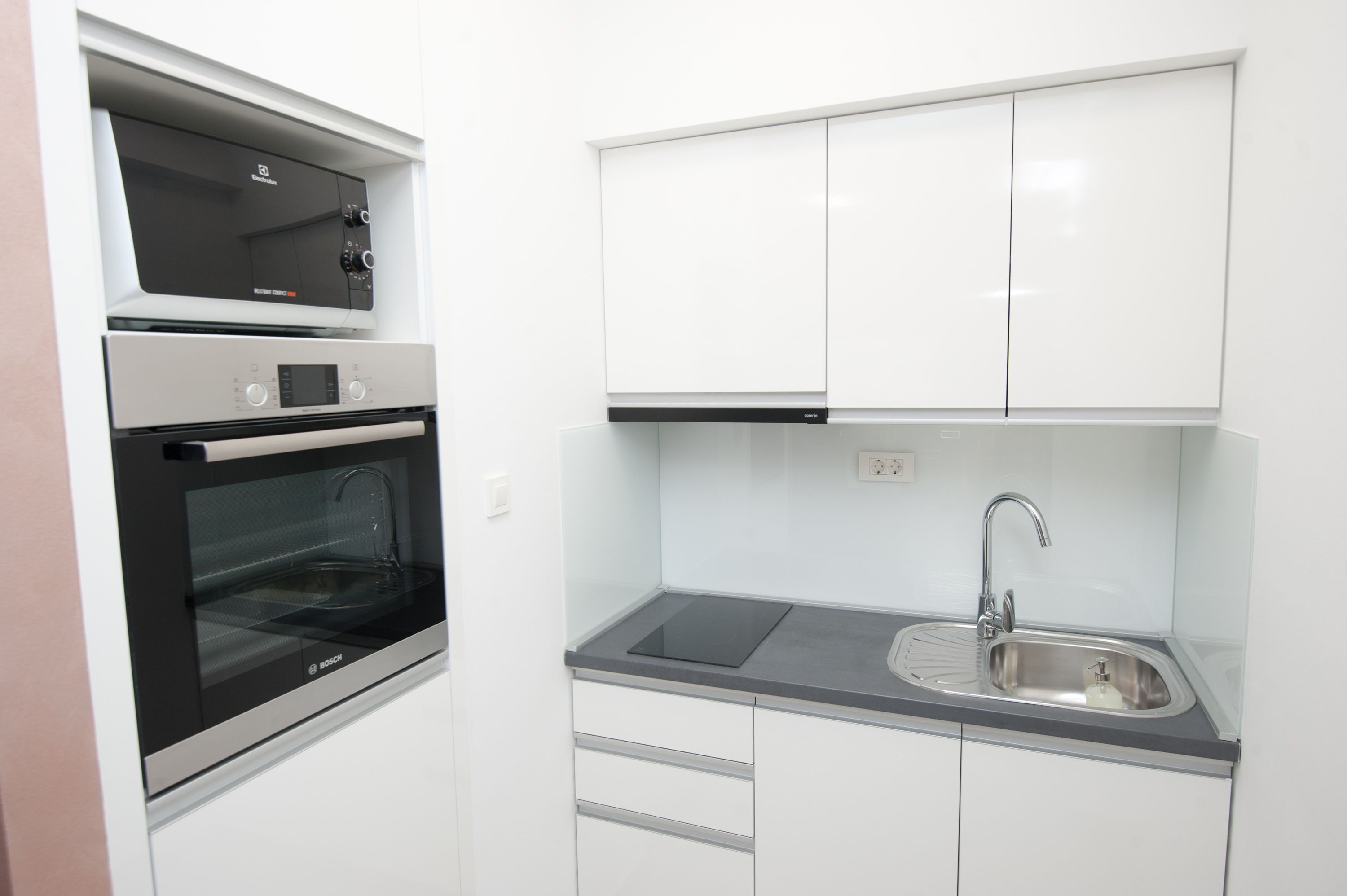 Una cocina compacta con horno Bosch, un lavamanos y armarios blancos.