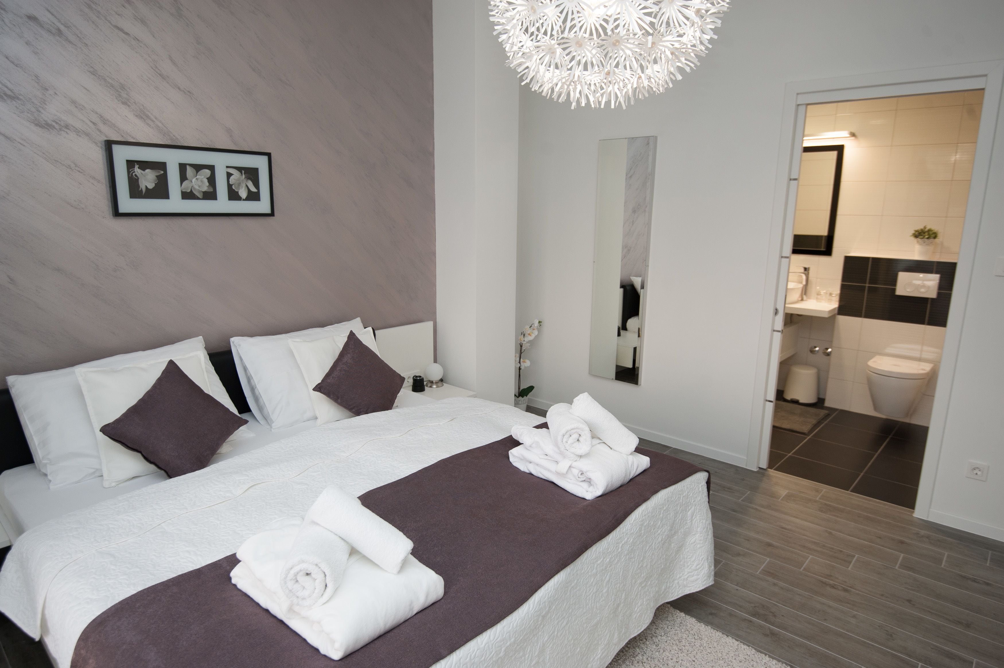 Habitación de hotel moderna con una cama grande, un baño a la vista a través de una puerta abierta y un candelabro único.