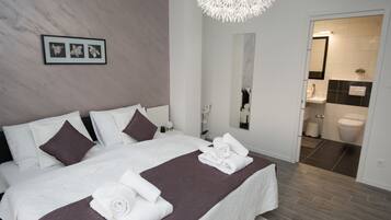 Habitación de hotel moderna con una cama grande, un baño a la vista a través de una puerta abierta y un candelabro único.