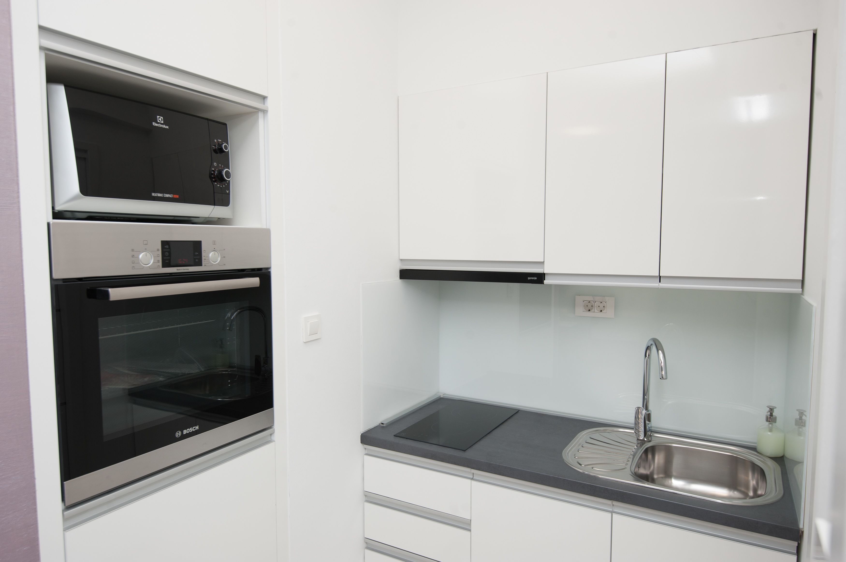 Una cocina compacta con horno Bosch, un lavamanos y armarios blancos.
