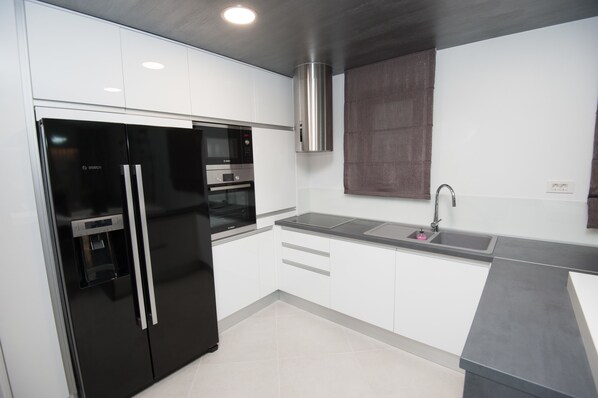 Una cocina moderna con armarios blancos, un refrigerador negro, una campana extractora de acero inoxidable y una encimera gris.