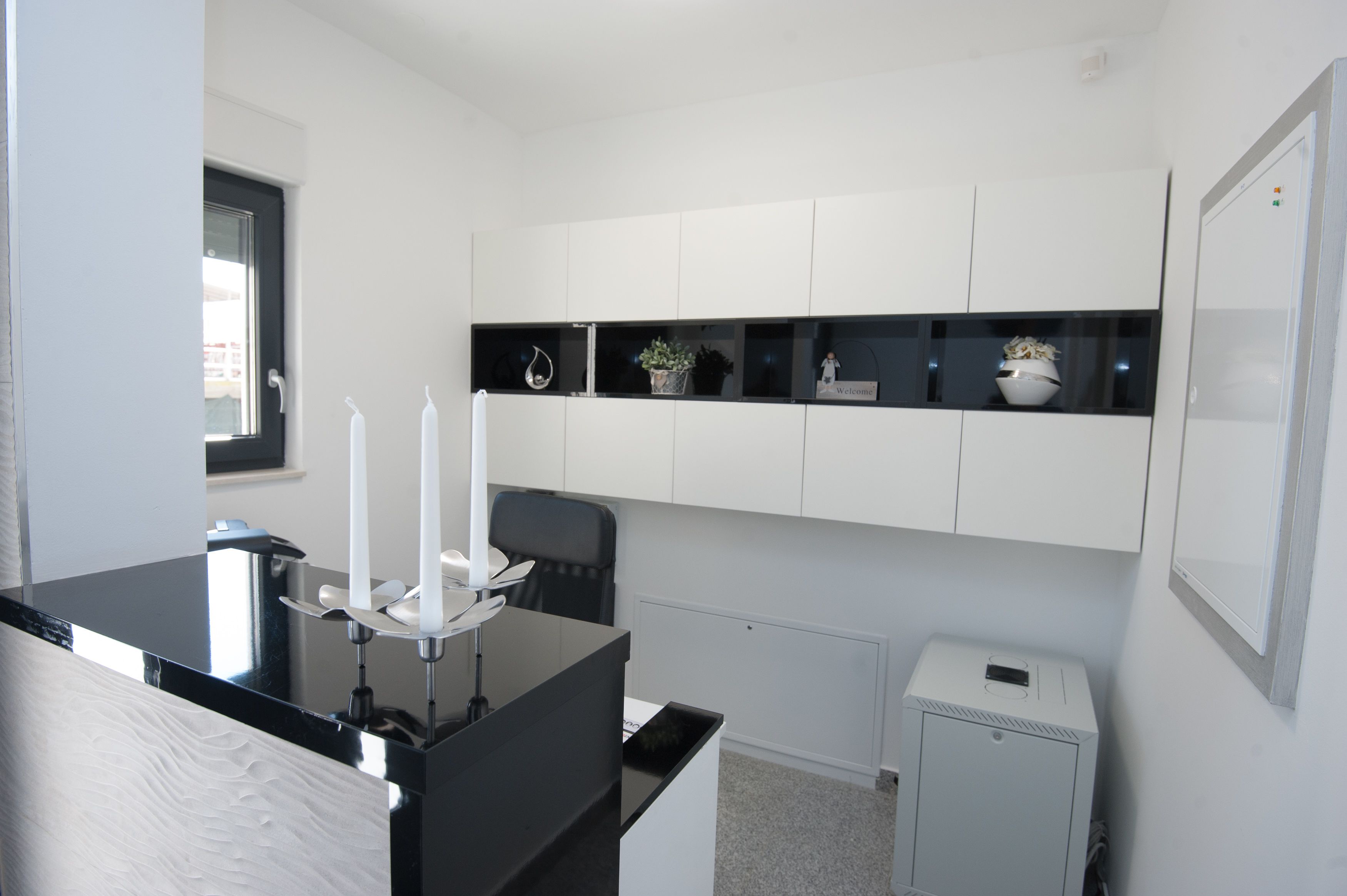 Un espacio de oficina moderno con un escritorio negro, armarios blancos y un pequeño radiador.