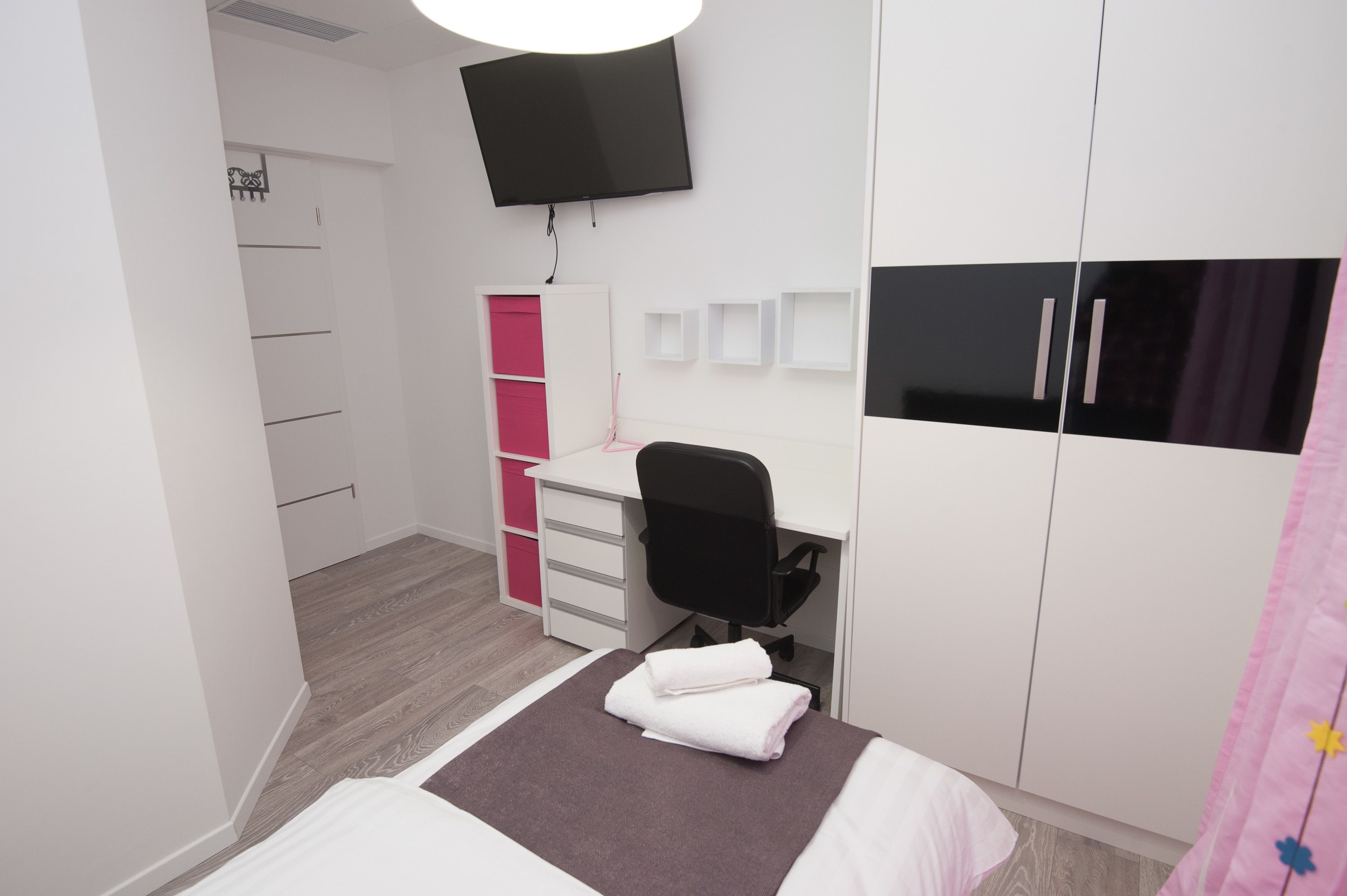Un dormitorio con cama, escritorio, silla, armario y televisor.