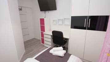 Un dormitorio con cama, escritorio, silla, armario y televisor.