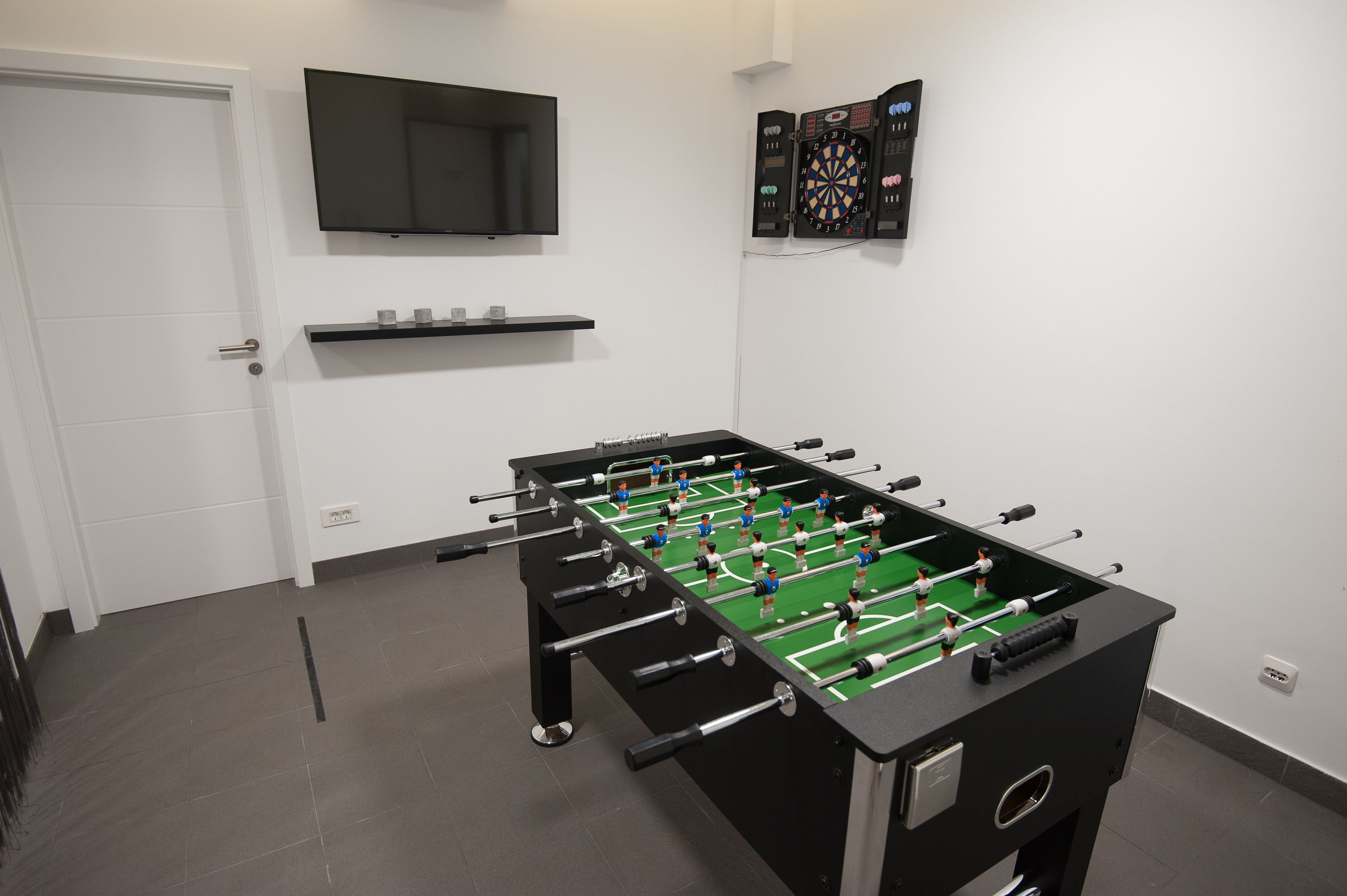 Una habitación con mesa de futbolín, televisor y dardos.