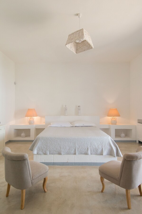 Camera da letto minimalista con un grande letto, due comodini con lampade e due poltrone.