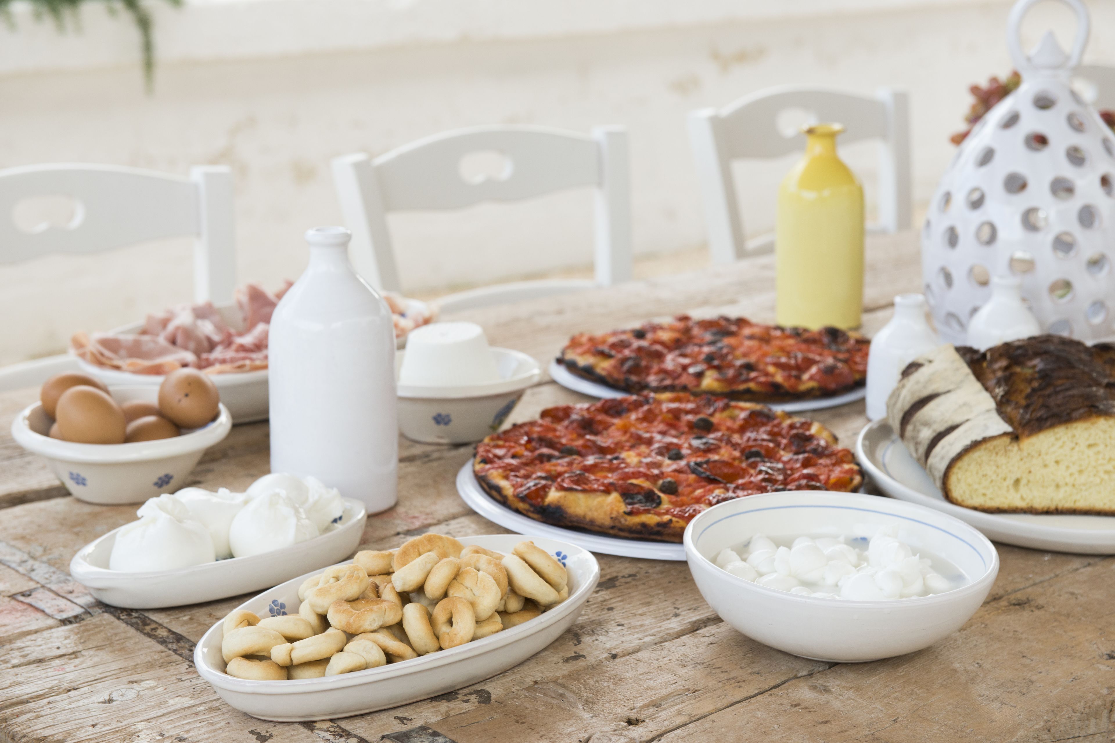 Una mesa con diversos alimentos, entre ellos huevos, pasteles y pizza.