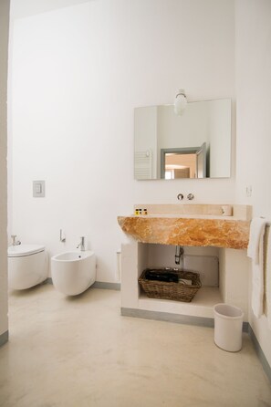 Un bagno moderno con un lavabo in marmo, due bidet, uno specchio e un piccolo cesto di vimini.