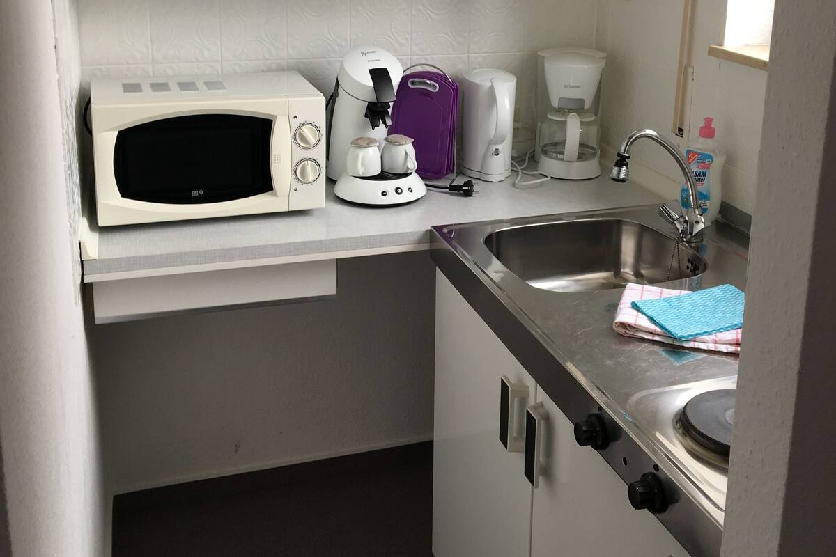 Eine kompakte Küchenzeile mit Mikrowelle, Kaffeemaschine und kleinem Spülbecken.