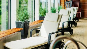A row of lounge chairs with white cushions and black frames, positioned in front of large windows with potted plants. - Harmonie Hotel Rust (Braunlage)