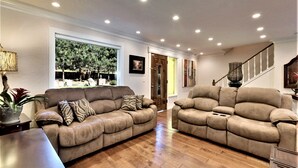 A spacious living room with two beige sofas, a wooden coffee table, and a large window offering a view of trees. - Zephyr Cove Versailles Private Beach & Ski Permitted DSTR1077P NV vacation House (Glenbrook)