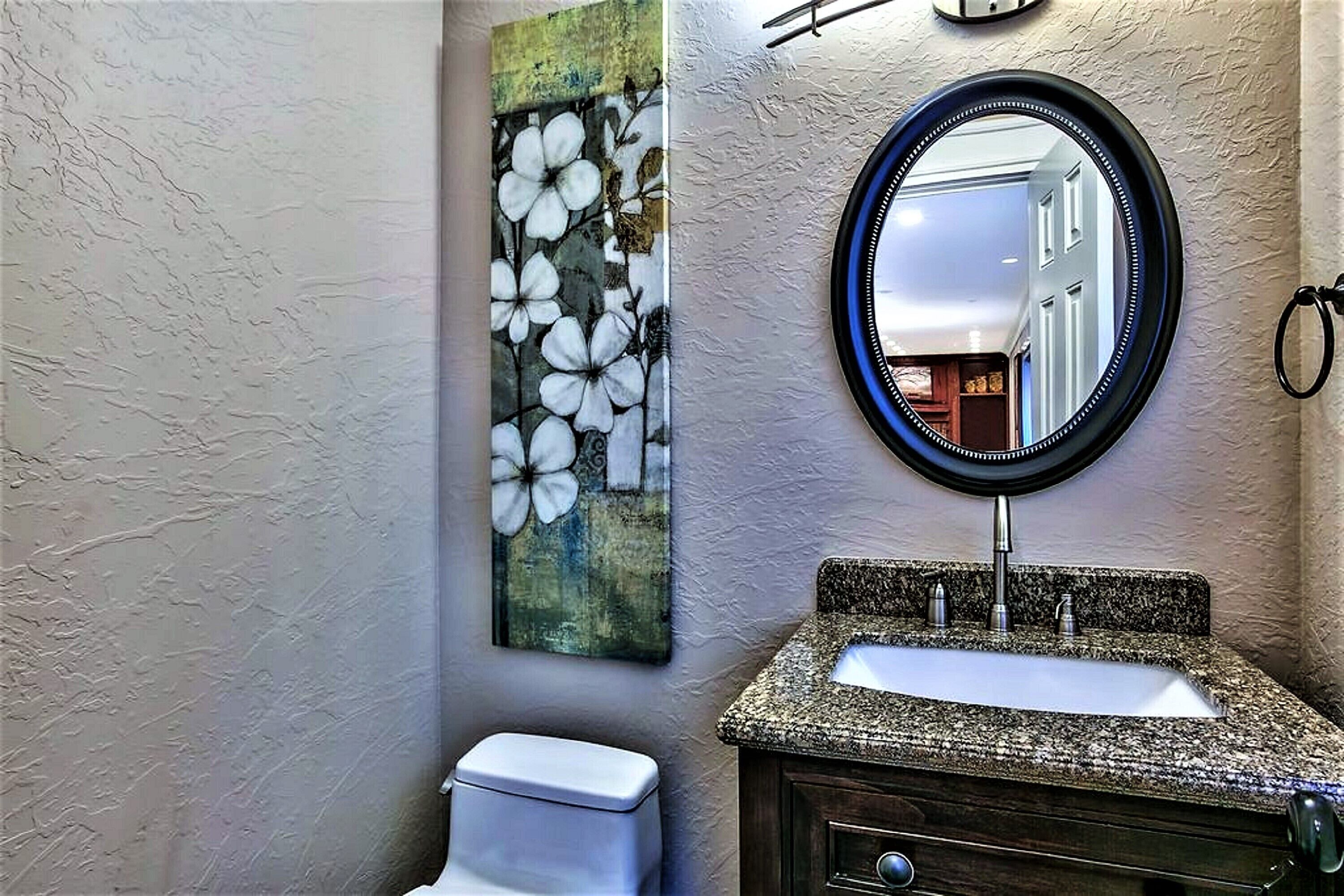 Une salle de bain avec un lavabo à vasque en granit, des toilettes blanches et un miroir fixé au mur.