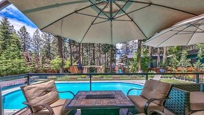An outdoor pool area with lounge chairs and a table, surrounded by trees and a view of a residential area. - Zephyr Cove Versailles Private Beach & Ski Permitted DSTR1077P NV vacation House (Glenbrook)