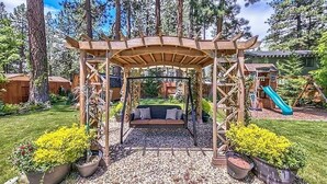 A wooden pergola with a swing set underneath, surrounded by a garden with potted plants and a slide. - Zephyr Cove Versailles Private Beach & Ski Permitted DSTR1077P NV vacation House (Glenbrook)