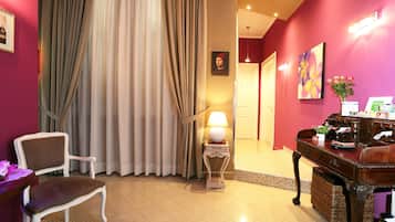 Una camera d'albergo con una sedia, un tavolo con una lampada, una scrivania con un vaso di fiori e un quadro appeso al muro.