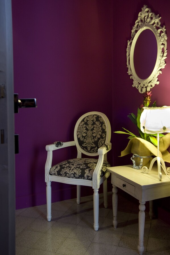 A room with a purple wall, a white chair with a patterned cushion, a white vanity with a mirror, and a small plant. - Antonello da Messina (Messina)