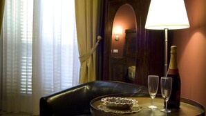 A hotel room with a leather sofa, a table with a bottle of champagne and two glasses, a lamp, and a window with curtains.