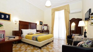 A hotel room with a bed, a desk, a chair, a TV, and a window with curtains.