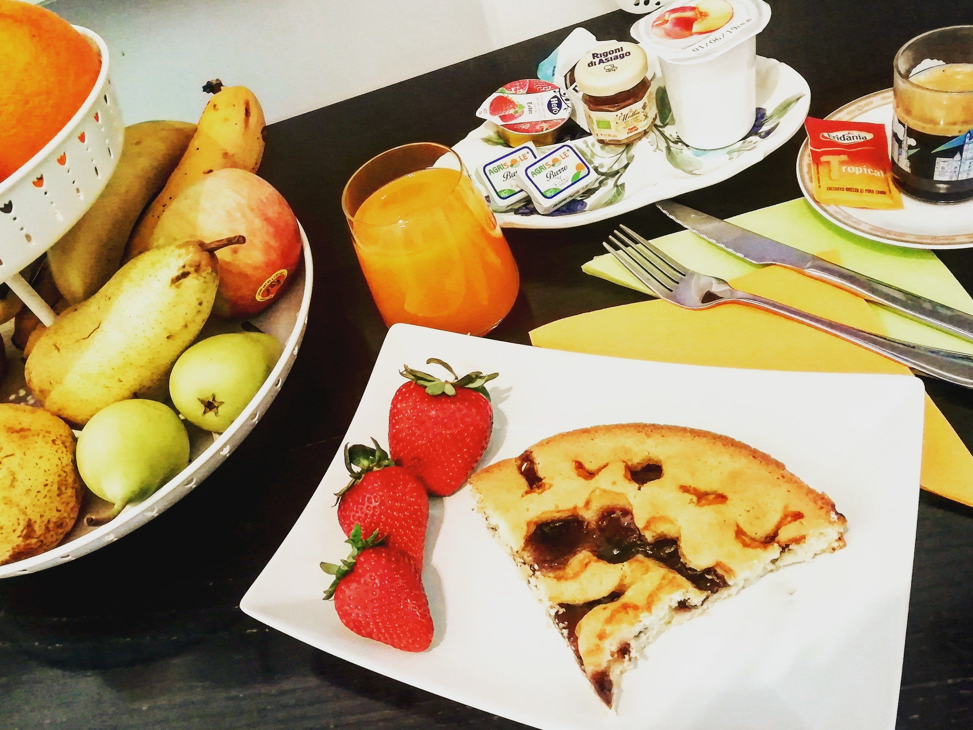 A breakfast setting with a plate of strawberries and a slice of pizza, a bowl of fruits, a cup of coffee, and condiments.
