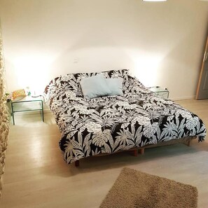 Ein Bett mit schwarz-weiß gestreifter Bettdecke, einem hellblauen Kissen und einem Glastischchen mit einer kleinen Pflanze.