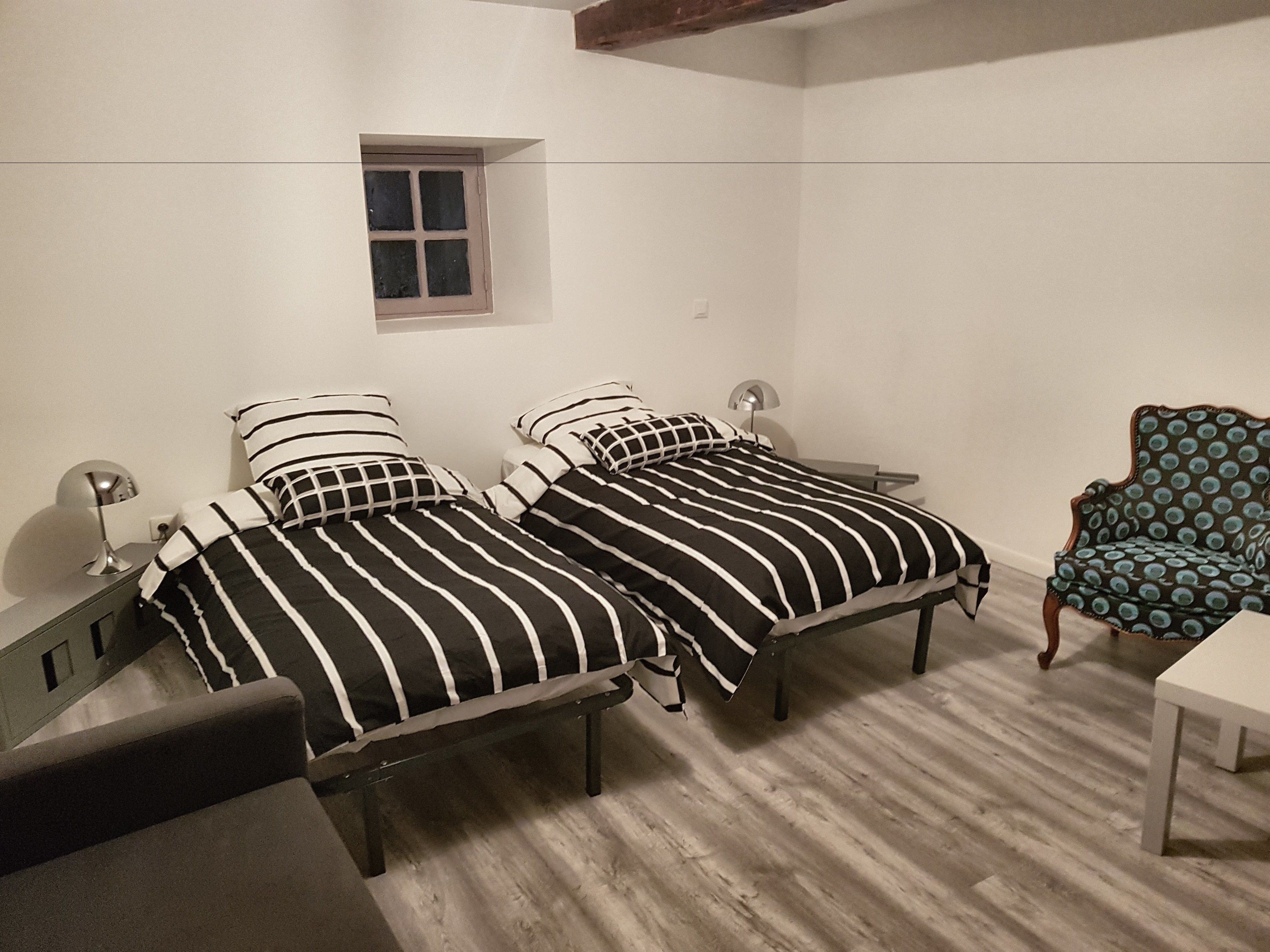 A bedroom with two beds, a small window, a chair, and a desk.