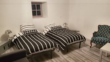 A bedroom with two beds, a small window, a chair, and a desk.