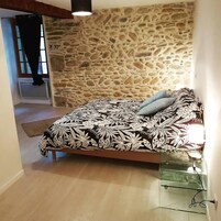 A bedroom with a stone wall, a bed with a floral bedspread, a glass bedside table, and a window with curtains.