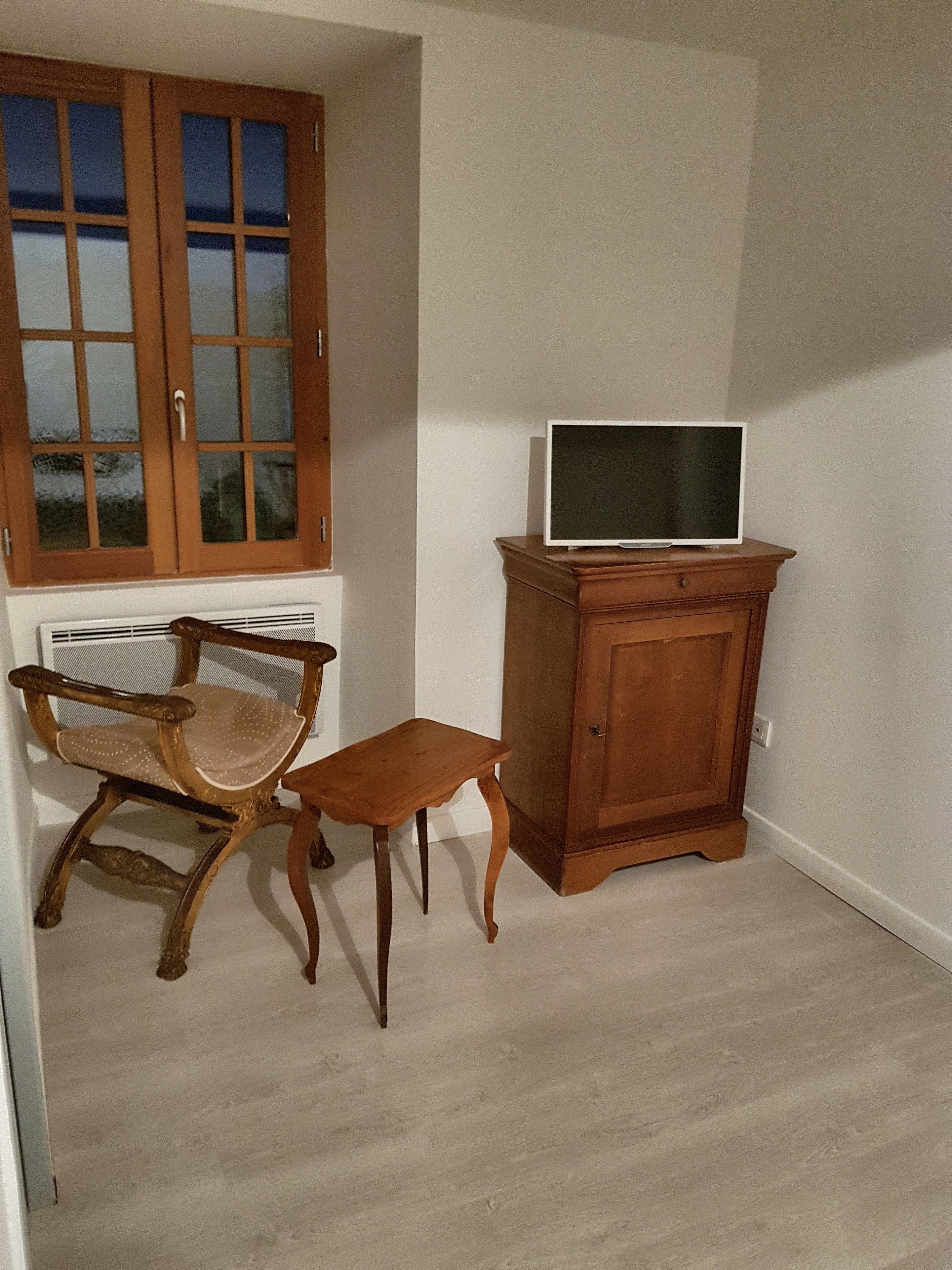 Een kamer met een houten kast, een televisie erboven, een stoel en een kleine tafel.