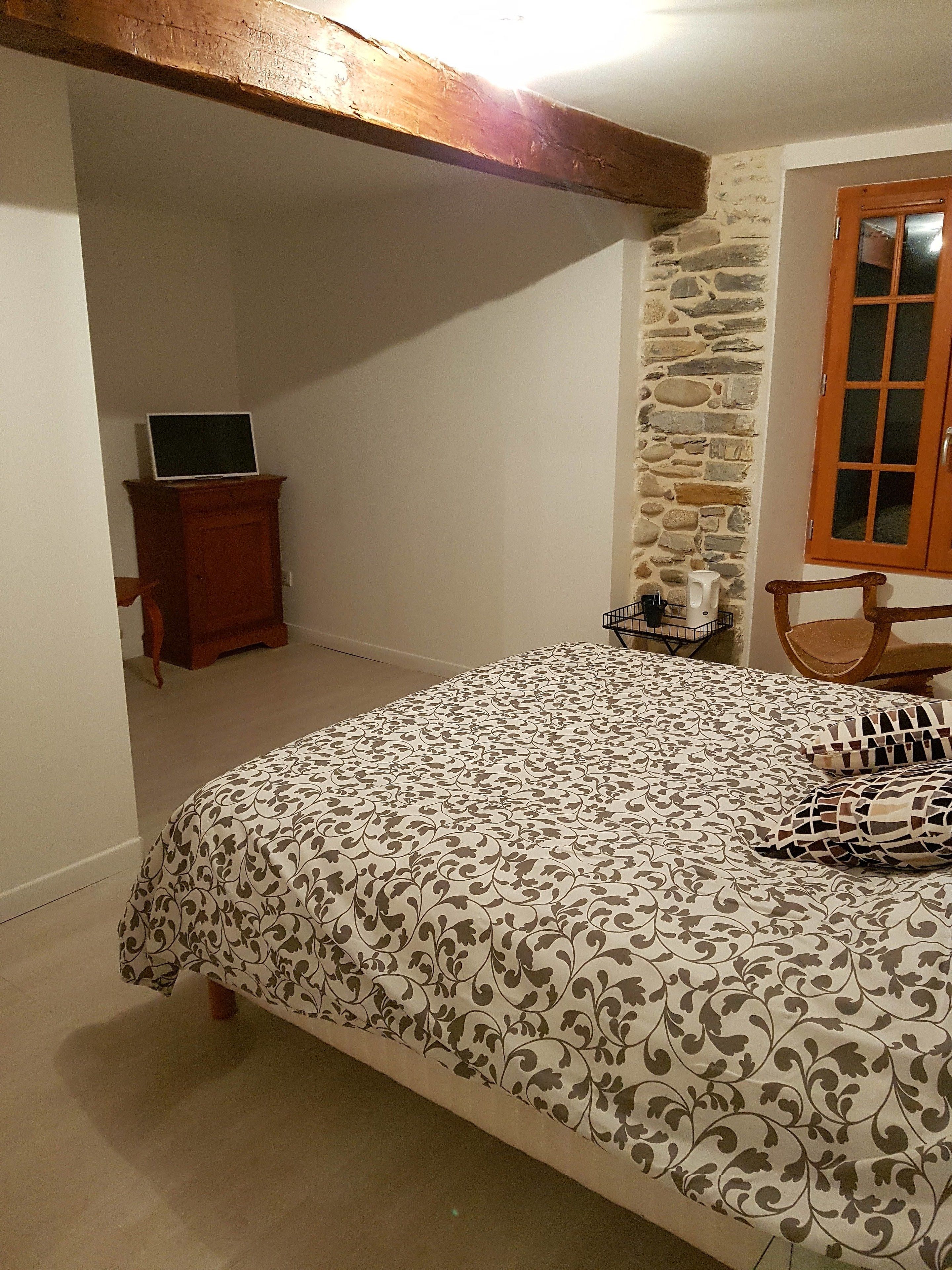 Ein Schlafzimmer mit einem Bett, einem Holzstuhl, einem kleinen Holzschrank, einer Steinwand und einem Fenster mit Holzläden.
