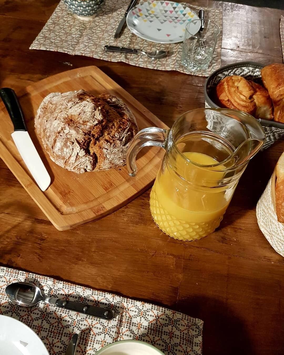 Uma mesa de madeira com um pão, um jarro de suco e um prato de croissants.