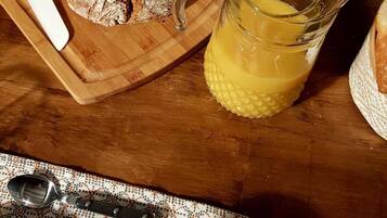 Uma mesa de madeira com um pão, um jarro de suco e um prato de croissants.