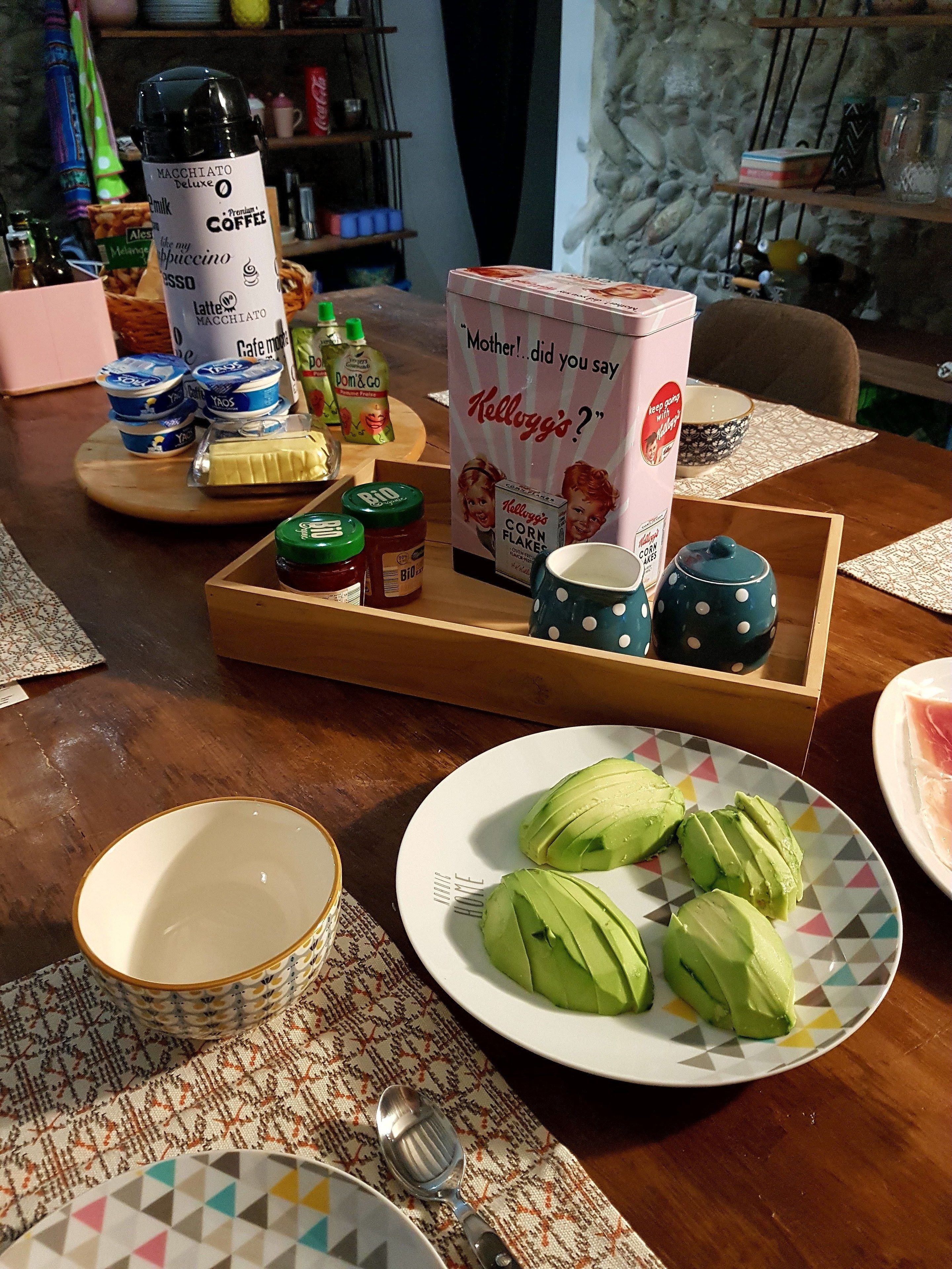 Een eettafel met eten, een koffiezetapparaat en een doos Kellogg's Corn Flakes.