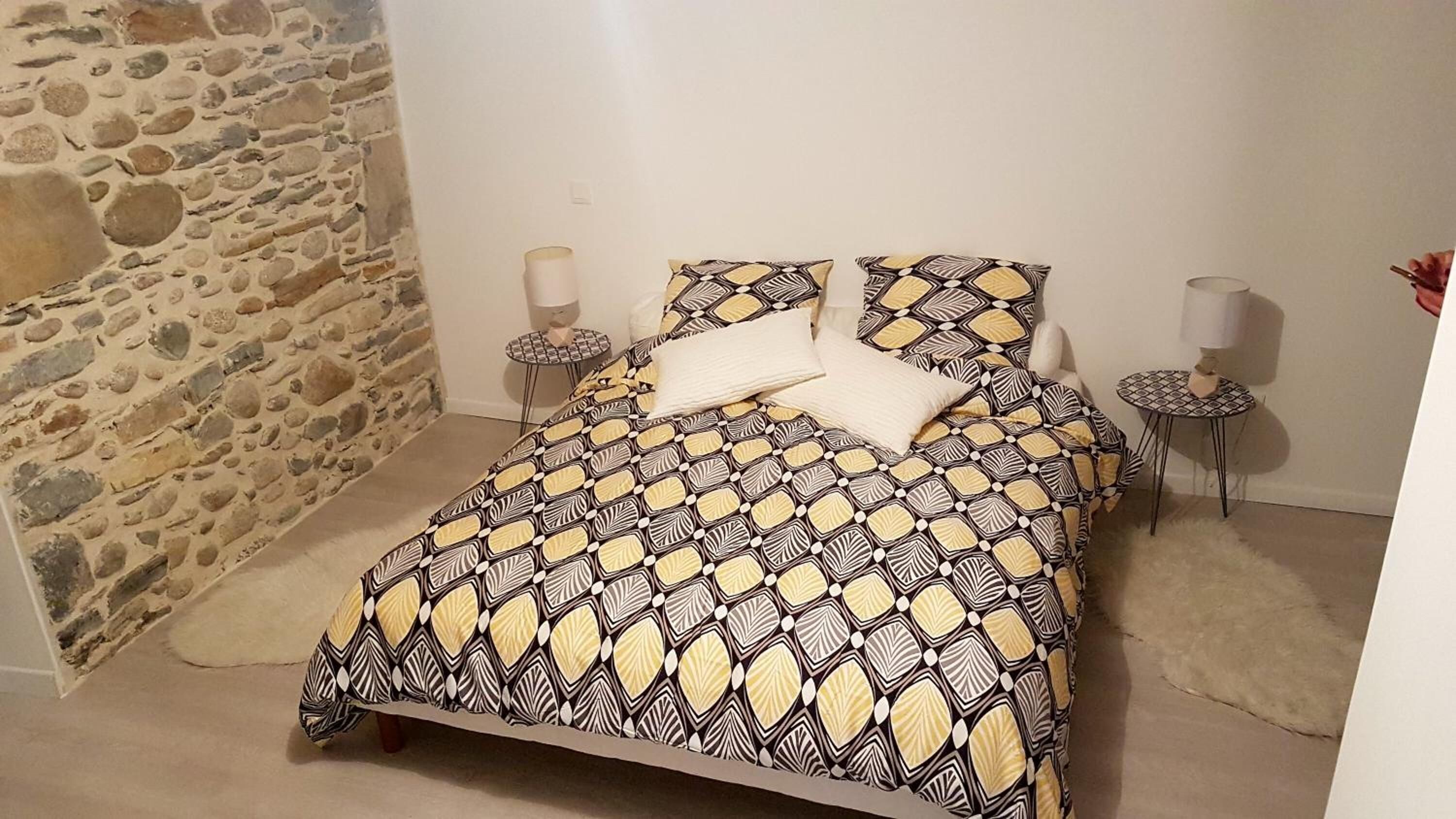 A bed with a patterned bedspread, two bedside tables with lamps, and a stone wall.