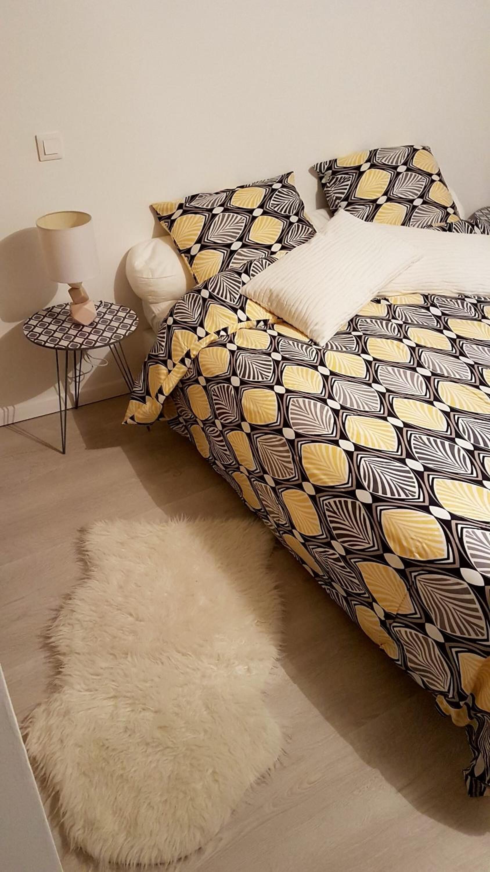 A bedroom with a patterned bedspread, a fluffy rug, and a side table with a lamp.