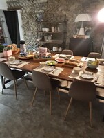 A dining area with a stone wall, a wooden table set for four, and a shelf with kitchen items in the background.