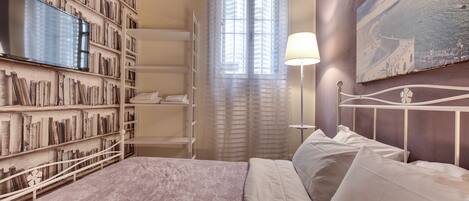 A bedroom with a bed, a bookshelf, a painting, and a window with curtains.
